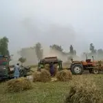 A field with tractors working in a dusty environment.
