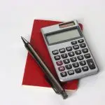 A calculator with a pen and red folder on a white surface.