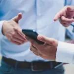 A person in a blue shirt holding a smartphone while discussing something.