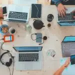 A busy desk with multiple people working on laptops.