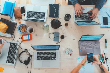 A busy desk with multiple people working on laptops.