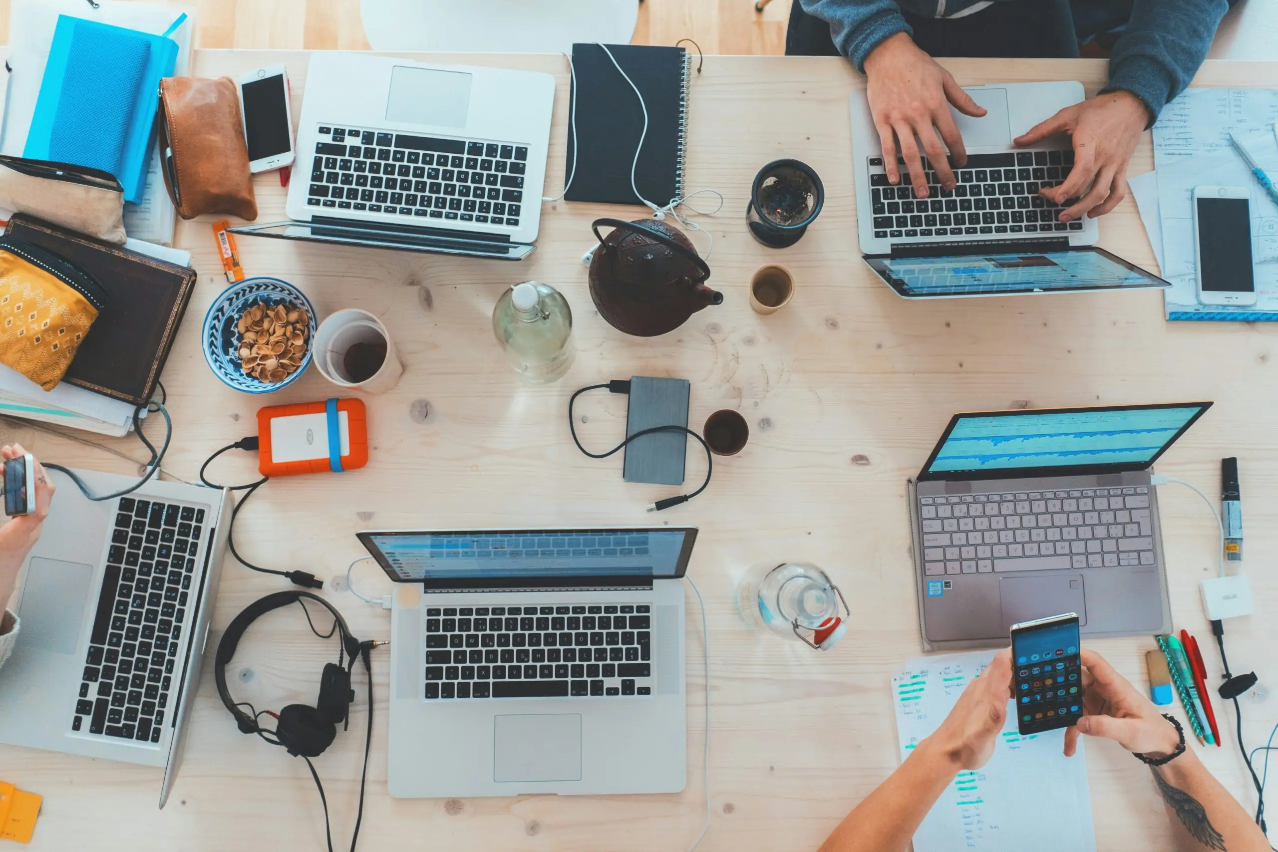 A busy desk with multiple people working on laptops.