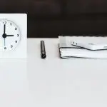 A white desk with a clock, pen, and tax documents.