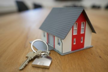 A miniature house model with keys on a wooden table.